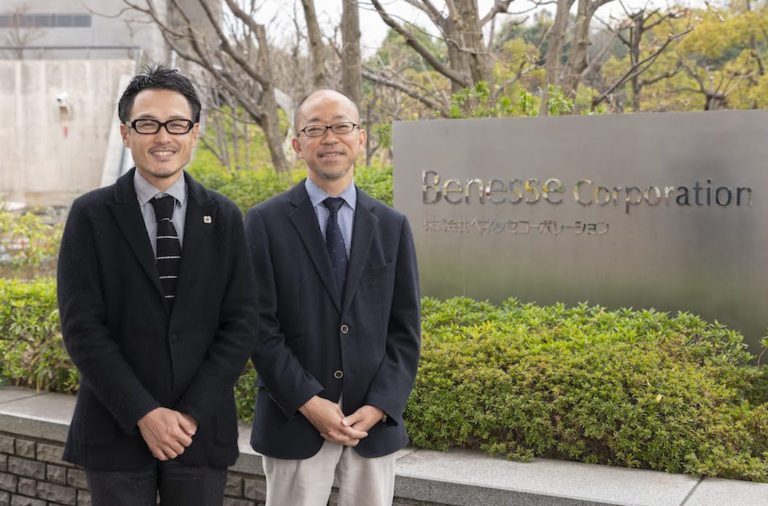 会社ロゴの前で立っているベネッセコーポレーションの男性社員2人