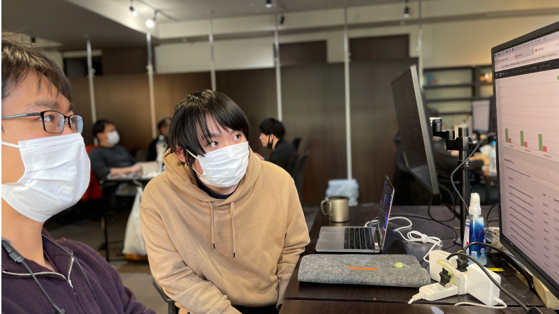 隣にいる吉田康平のパソコン画面を見て話しているマスク姿の木下航