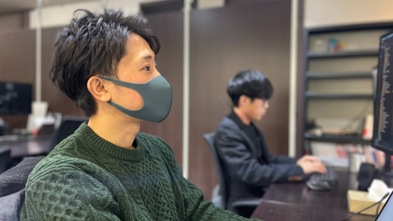 グレーのマスクをした男性（和田一真）が座ってパソコンをしている右横顔